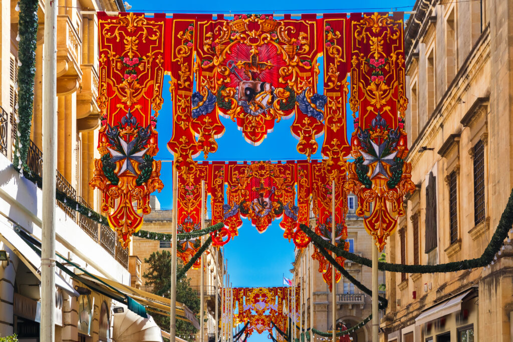 Festively decorated street with banners for St Augustine Feast in the old town of Valletta, Malta. Flaming, arrow pierced heart - symbol of St Augustine
